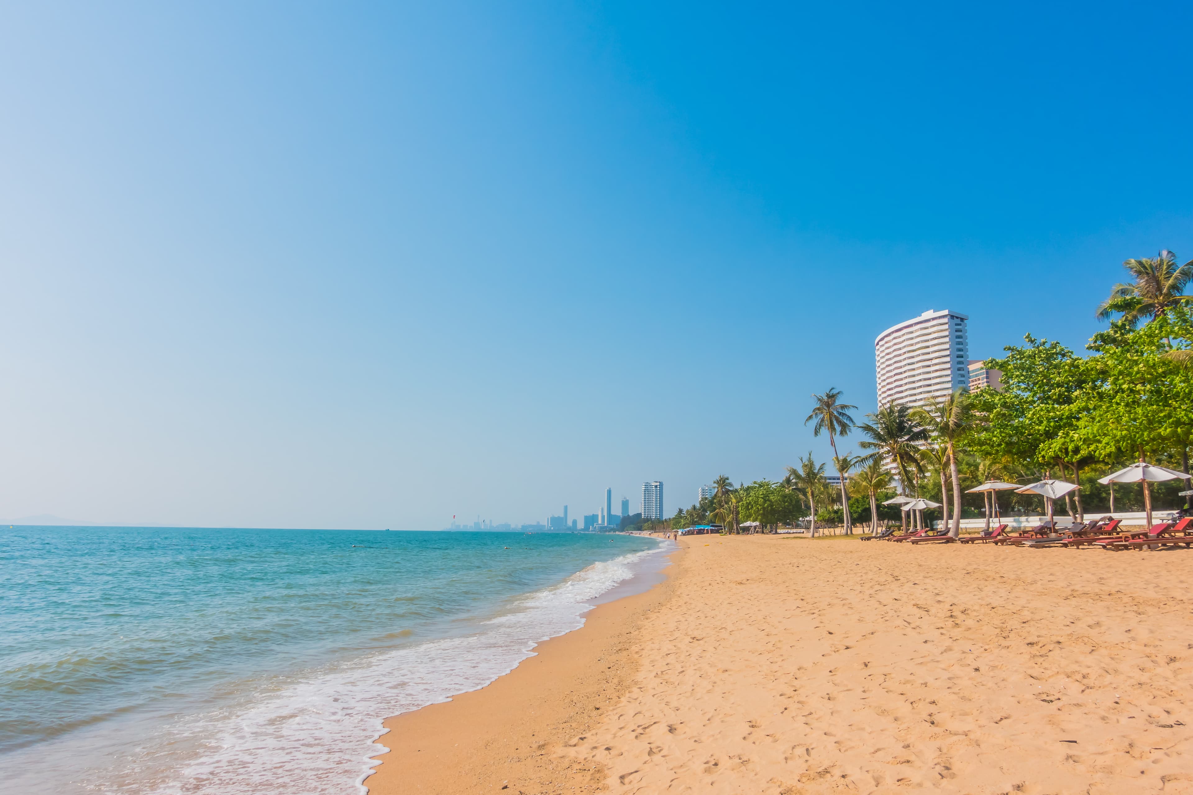 Tropical sandy beach with turquoise water, palm trees, and a tall white hotel building.